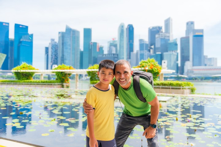 Man and boy smiling in front of skyscrapers and water lilies.