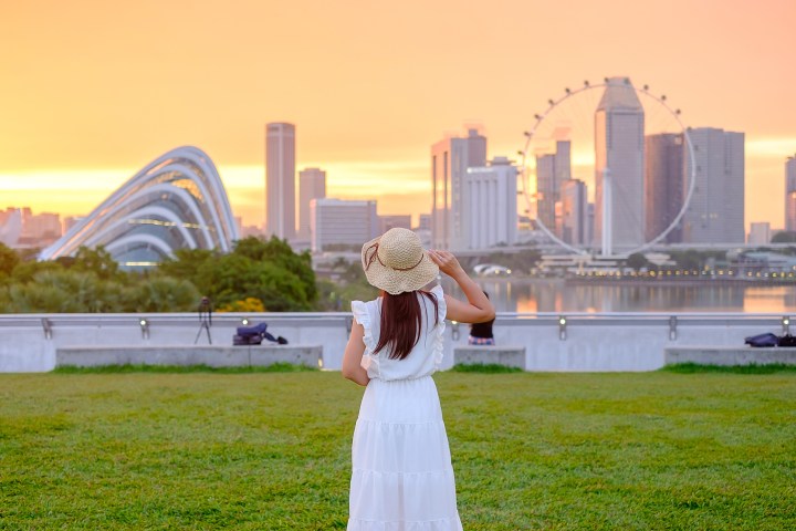 Woman in white dress and hat looks at city skyline during sunset.