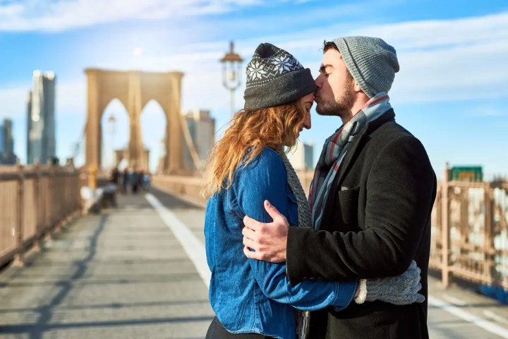 Couple embracing and kissing on Brooklyn Bridge, wearing winter clothes.