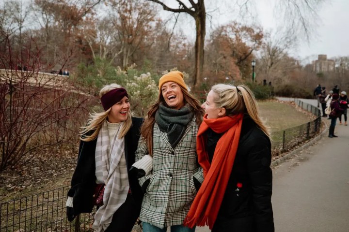 Three women laughing while walking in a park during winter.