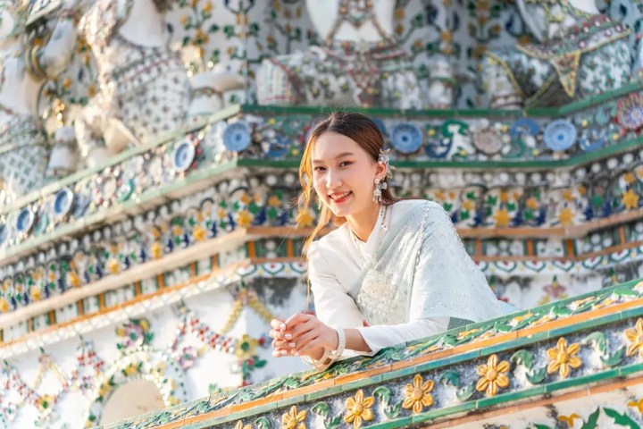 Woman in traditional attire smiling by intricate temple with colorful floral patterns.