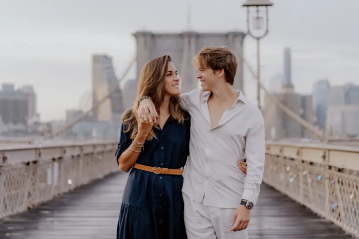 Couple walking arm in arm on a bridge with city skyline in the background.